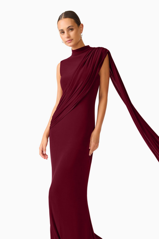 Elliatt Tuloria Sash Gown in Burgundy Red featuring an elegant floor-length silhouette, high neckline, sleeveless design, and dramatic asymmetric draped sash.