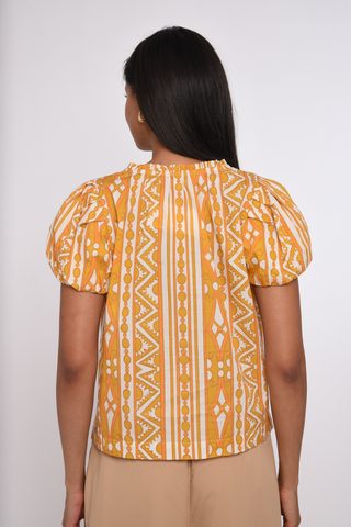 Model wearing the Love the Label Lia Top in Bowen Deco Print featuring puff sleeves and a golden geometric print.