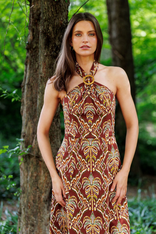 Model wearing the Shoshanna Lainey Dress in Bronze Multi featuring a halter neckline, wooden buckle, fitted bodice, and printed A-line midi skirt.
