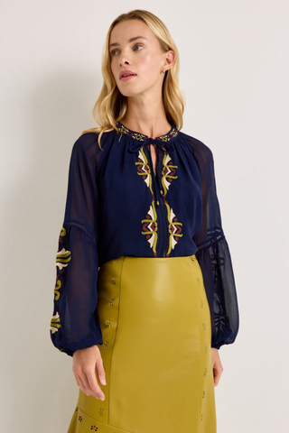 Marie Oliver Royce Blouse in Sundown featuring deep navy fabric, colorful embroidery, a tie neckline, and billowy sleeves.