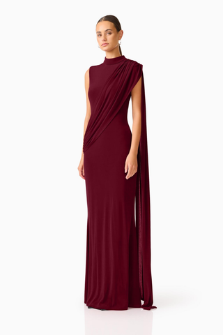 Elliatt Tuloria Sash Gown in Burgundy Red featuring an elegant floor-length silhouette, high neckline, sleeveless design, and dramatic asymmetric draped sash.