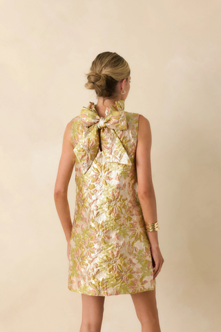 Model wearing Prosperina Cecily Mini Dress in Bombshell Botanicals featuring floral jacquard fabric, ruffle neckline, and oversized bow back detail