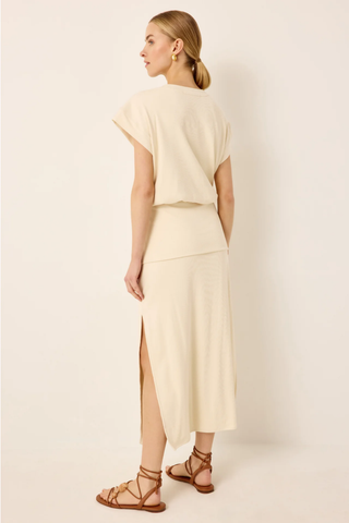 Woman wearing a light-colored outfit with a slit skirt on a plain background