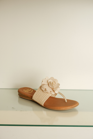 Andre Assous Nara Sandal in natural featuring a woven raffia-inspired upper, floral appliqué detail, and cushioned thong sandal silhouette