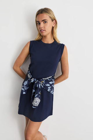 Woman wearing a navy dress with a floral patterned belt against a white background