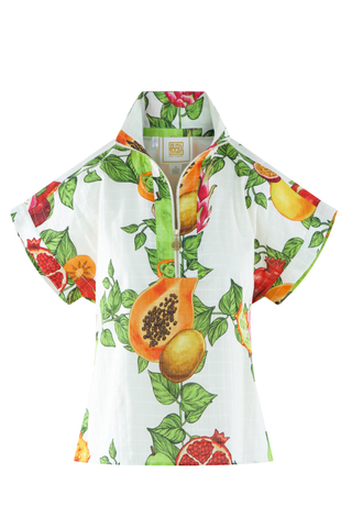 Model wearing the Emily McCarthy Poppy Pullover in Trellis Grove featuring a colorful tropical fruit print, cap sleeves, stand collar, and gold zip neckline