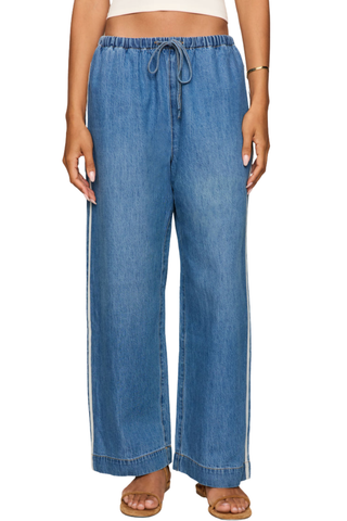 Model wearing the Z Supply Sidelines Denim Track Pant in Dreamstate featuring wide-leg denim, pull-on waistband, and tie-front detail.