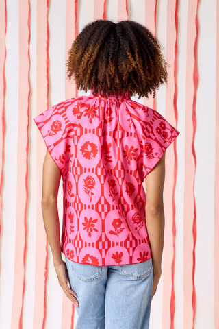 Model wearing Crosby Wilkes Top in Parterre Floral featuring pink and red floral print, flutter sleeves, and a ruffled mock neckline