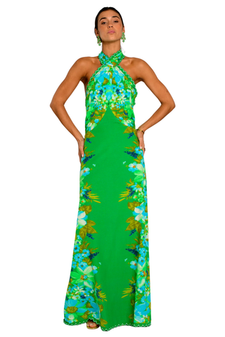 Model wearing the Elizabeth James the Label Aubrey Dress in Hula featuring a vibrant green tropical floral print, criss cross halter neckline, open smocked back, scallop trim detailing, and flowing maxi silhouette styled for a tropical resort setting