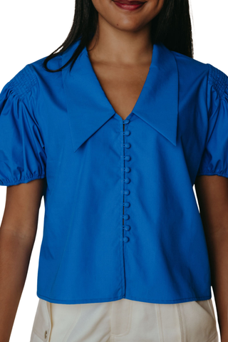 Blue blouse with short sleeves worn by a person on a white background