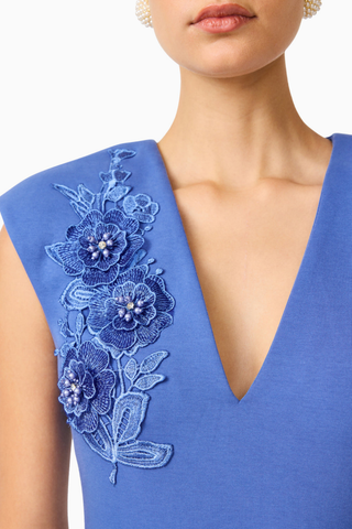 Model wearing the Elliatt Talitha Maxi Dress in Cornflower Blue featuring a plunging V-neckline, structured shoulders, floral appliqué detailing, and a slim column silhouette.