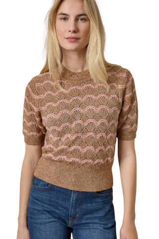 A woman wearing a short-sleeve knit sweater with a wavy, scalloped pattern in tan and dusty pink, paired with blue jeans, against a plain white background.