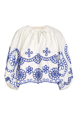 Model wearing the Marie Oliver Vara Top in Bluejay, an ivory cotton blouse featuring cobalt blue embroidered eyelet detailing, a tie neckline, puff sleeves, scalloped hem, and a relaxed silhouette.