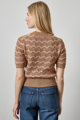 Woman wearing a brown patterned sweater and blue jeans on a plain background