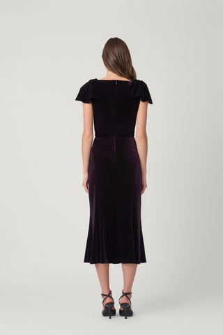 Shoshanna Brandis Dress in Dark Plum featuring stretch velvet, a boat neckline, draped bow shoulders, fitted bodice, and softly flared midi skirt.
