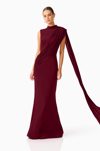 Elliatt Tuloria Sash Gown in Burgundy Red featuring an elegant floor-length silhouette, high neckline, sleeveless design, and dramatic asymmetric draped sash.