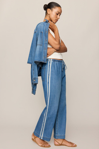 Model wearing the Z Supply Sidelines Denim Track Pant in Dreamstate featuring wide-leg denim, pull-on waistband, and tie-front detail.