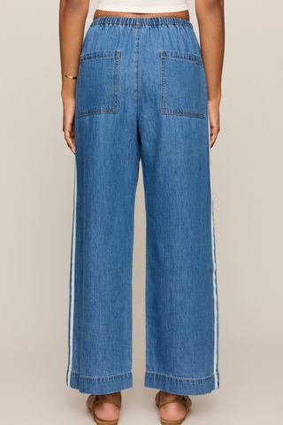 Model wearing the Z Supply Sidelines Denim Track Pant in Dreamstate featuring wide-leg denim, pull-on waistband, and tie-front detail.
