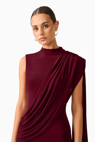 Elliatt Tuloria Sash Gown in Burgundy Red featuring an elegant floor-length silhouette, high neckline, sleeveless design, and dramatic asymmetric draped sash.