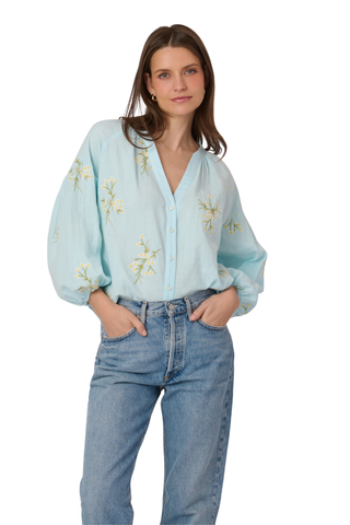 Woman wearing a light blue blouse with floral embroidery and jeans on a white background
