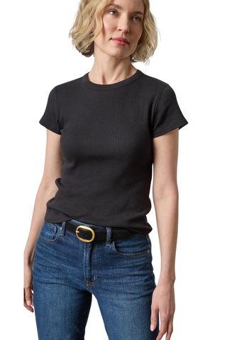 A woman wearing a black short-sleeve ribbed crewneck t-shirt and blue jeans with a gold-buckled belt, photographed against a plain white background.