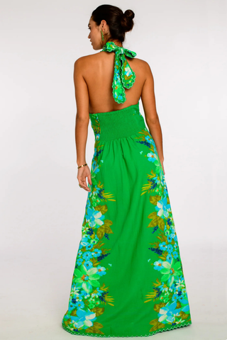 Model wearing the Elizabeth James the Label Aubrey Dress in Hula featuring a vibrant green tropical floral print, criss cross halter neckline, open smocked back, scallop trim detailing, and flowing maxi silhouette styled for a tropical resort setting