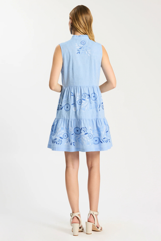 Woman wearing a light blue dress with floral embroidery on a white background