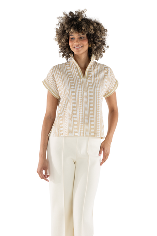 Woman wearing a beige embroidered top and white pants on a white background