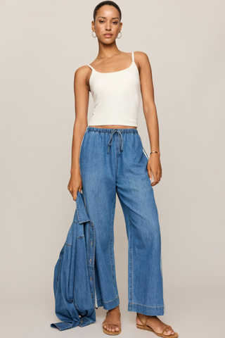 Model wearing the Z Supply Sidelines Denim Track Pant in Dreamstate featuring wide-leg denim, pull-on waistband, and tie-front detail.