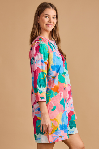 Model wearing the Double A Paloma Dress in Bougainville featuring a colorful watercolor floral print, button-front styling, three-quarter sleeves, and a relaxed mini silhouette