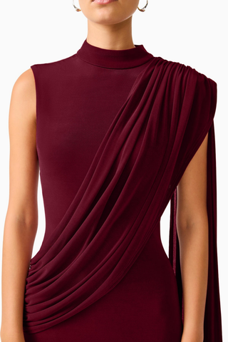 Elliatt Tuloria Sash Gown in Burgundy Red featuring an elegant floor-length silhouette, high neckline, sleeveless design, and dramatic asymmetric draped sash.