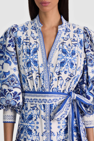 Model wearing the Alice + Olivia Cora Maxi Shirt Dress in Solstice featuring a blue-and-white porcelain-inspired print, blouson sleeves, adjustable tie waist, tiered maxi skirt, and lightweight cotton voile fabrication paired with flat sandals