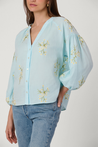 Light blue blouse with floral embroidery worn by a person on a white background
