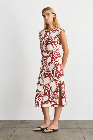 Woman wearing a sleeveless dress with a red and white abstract pattern on a plain background