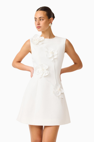 Model wearing the Elliatt Reina Mini Dress in White featuring a sleeveless silhouette, intricate 3D floral appliqué, and a structured A-line mini dress.