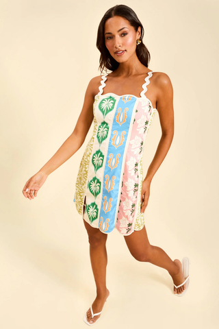 Model wearing Mestiza Sail Away Mini Dress in Beach Bazaar featuring ric rac straps, scalloped neckline, and colorful patchwork-inspired print