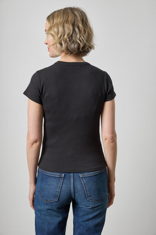 A woman with short blonde hair is shown from the back wearing a black short-sleeve ribbed t-shirt and blue jeans against a light gray studio background.