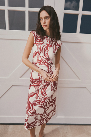 Woman wearing a red and white patterned dress standing against a white wall.