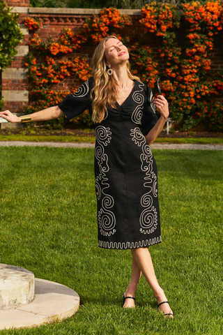 Model wearing Tyler Boe Posey Linen Midi Dress in black linen with white contrast embroidery, lantern sleeves, and midi silhouette