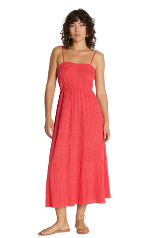 Model wearing the Nation LTD Madeline Tie Midi Dress in Flora, a coral pink textured midi dress featuring adjustable tie straps, shirred detailing, smocked voile fabric, a fitted bodice, and a flowing skirt.