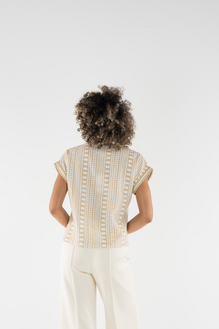 Person wearing a beige patterned top and white pants on a light gray background