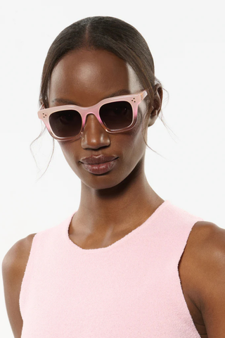 Woman wearing pink sunglasses and a matching dress against a white background