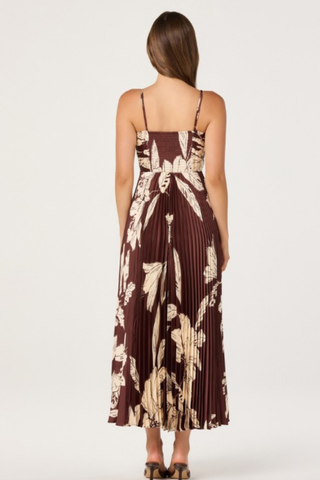 Model wearing the ASTR Clea Dress in Brown Floral featuring a gathered V-neck bodice, adjustable spaghetti straps, flowing pleated maxi skirt, and oversized cream floral print on a rich brown background.