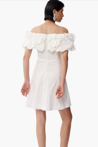 Model wearing De Loreta Cumaral Dress in White with off-the-shoulder ruffle sleeves, structured bodice, and fit-and-flare mini silhouette
