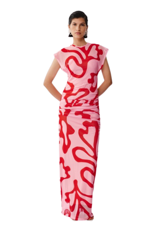Model wearing De Loreta Melodi Dress in Nory Pink with abstract red print, ruched detailing, cap sleeves, and open back maxi silhouette