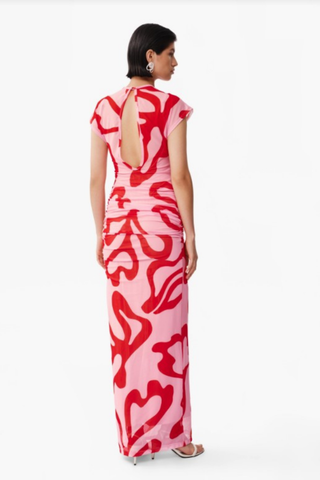 Model wearing De Loreta Melodi Dress in Nory Pink with abstract red print, ruched detailing, cap sleeves, and open back maxi silhouette