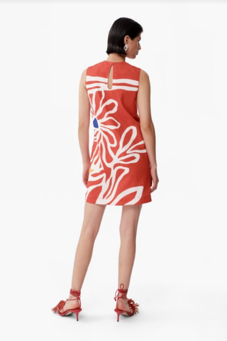 Model wearing De Loreta Mundo Dress in Miraflores with oversized ivory floral print, sleeveless shift silhouette, and coral red mini dress design