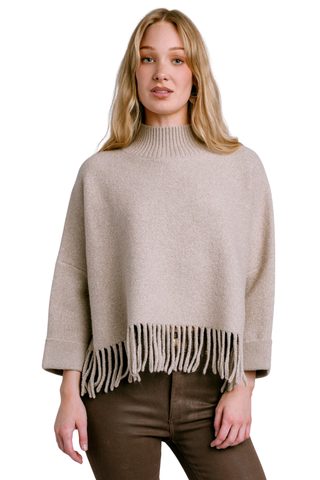 Kerisma Sachi Aja Sweater in Warm Wheat featuring a relaxed poncho silhouette, mock neckline, wide sleeves, and fringe trim.