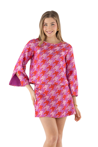 Emily McCarthy Ashley Ann Top in Houndstooth featuring a vibrant pink, red, and lavender pattern with flared sleeves and contrast trim.