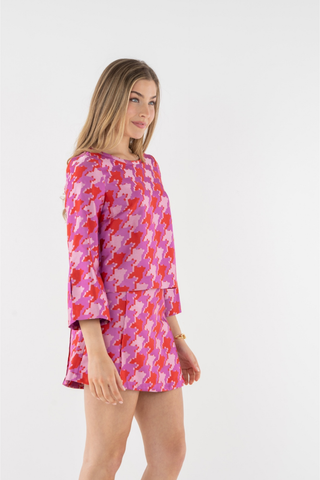 Emily McCarthy Ashley Ann Top in Houndstooth featuring a vibrant pink, red, and lavender pattern with flared sleeves and contrast trim.